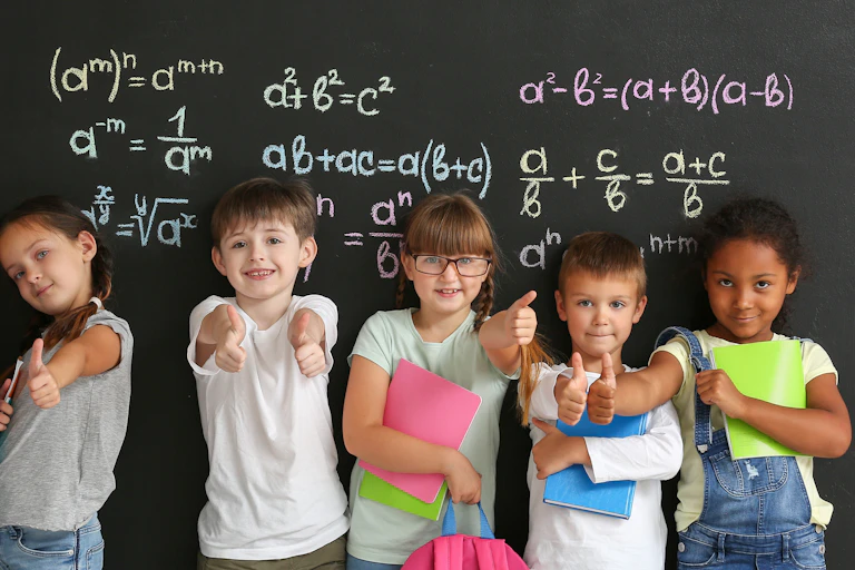 Des enfants dos à un tableau noir couvert de formules mathématiques.