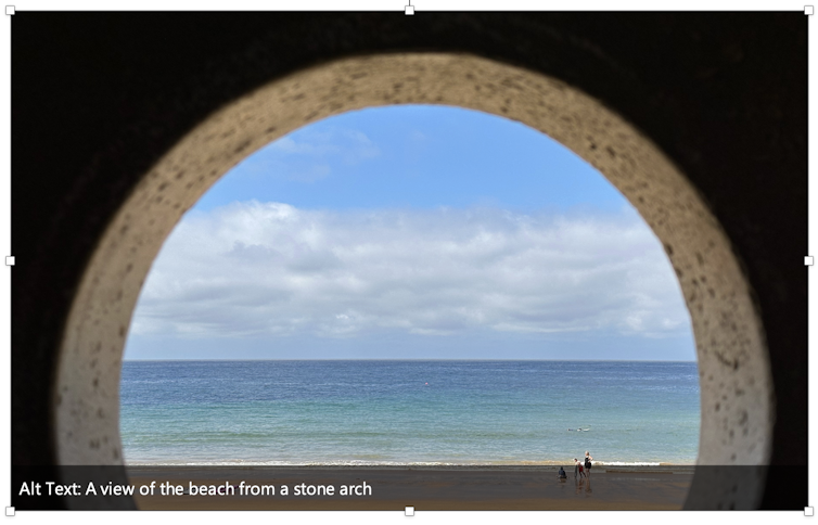 A screenshot of an image with the alt-text description that reads A view of the beach from a stone arch.