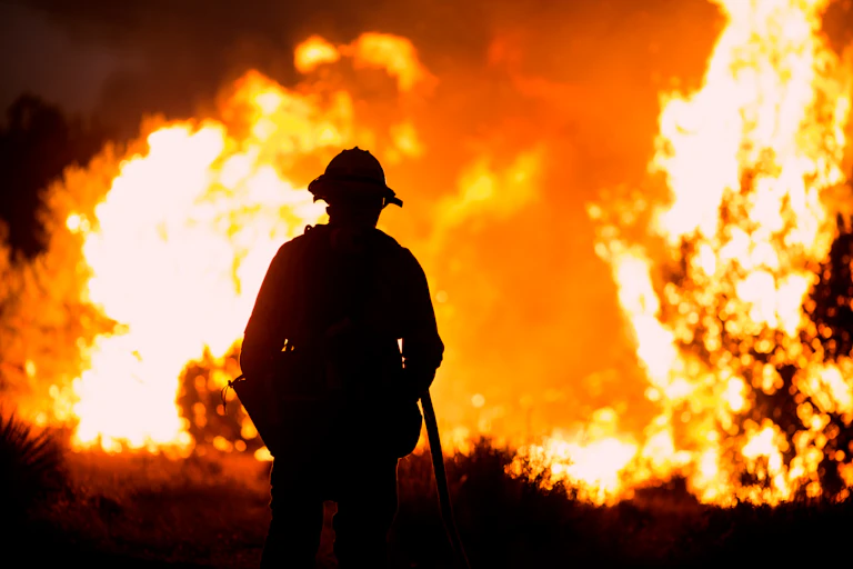 firefighter silhouetted in front of large fire