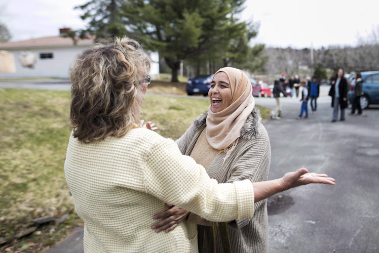 A woman in a niqab smiles joyously as she embraces another woman.