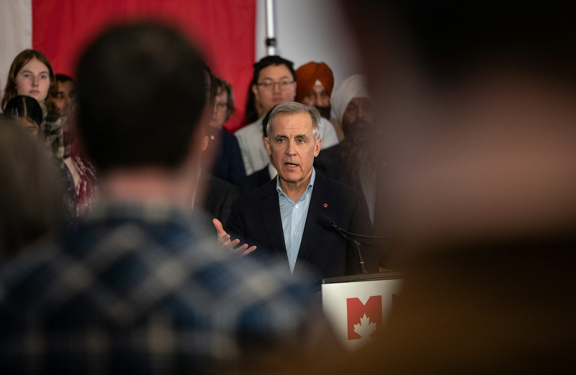 A grey-haired man is framed between journalists as he answers questions.