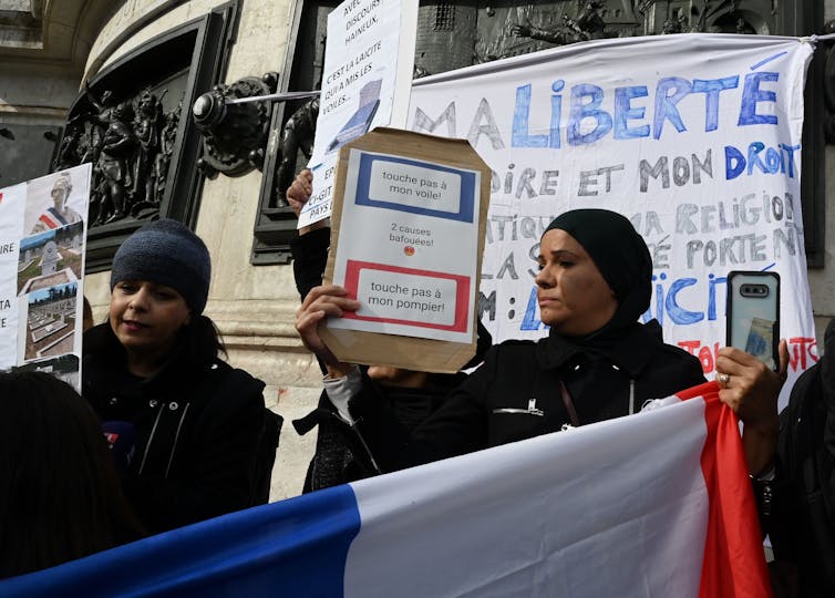 Women wearing headscarves hold signs that read, 'Don’t touch my headscarf.'