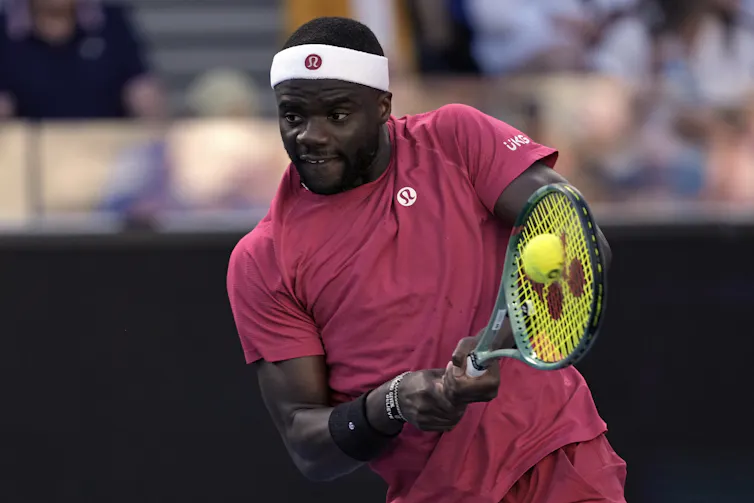 African American man wearing a red shirt playing tennis.