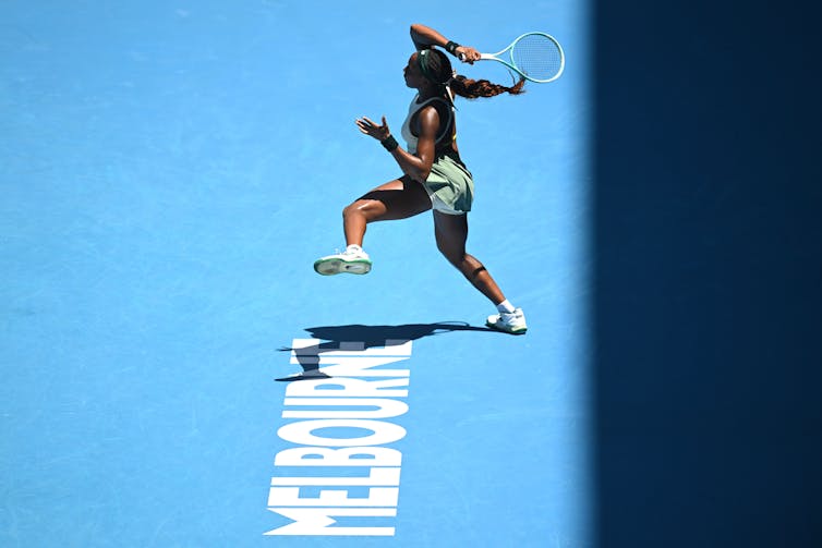 African American woman playing tennis on a blue court.