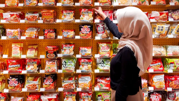 Indonesian woman picking Korean packaged instant noodles from supermarket shelf