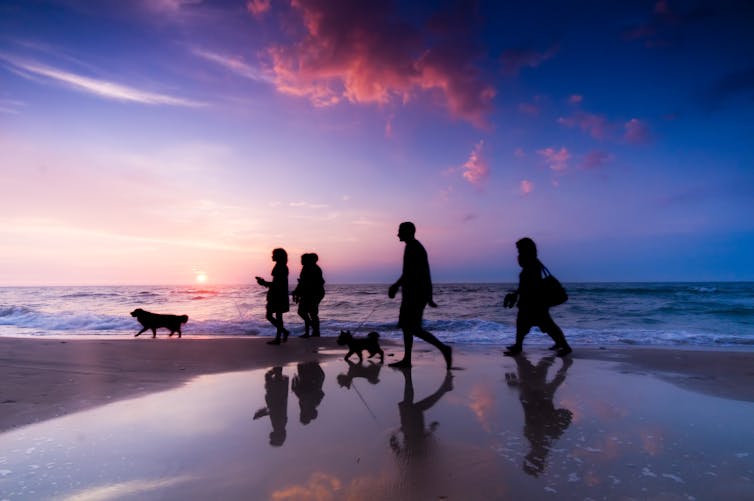 A family walks on a beach at sunset.
