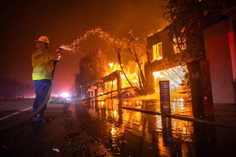 A firefighter battles the Palisades Fire while it burns homes at Pacific Coast Highway.