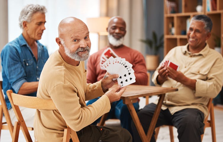 Four men playing cards at a table, with the man in the foreground turned to face the camera