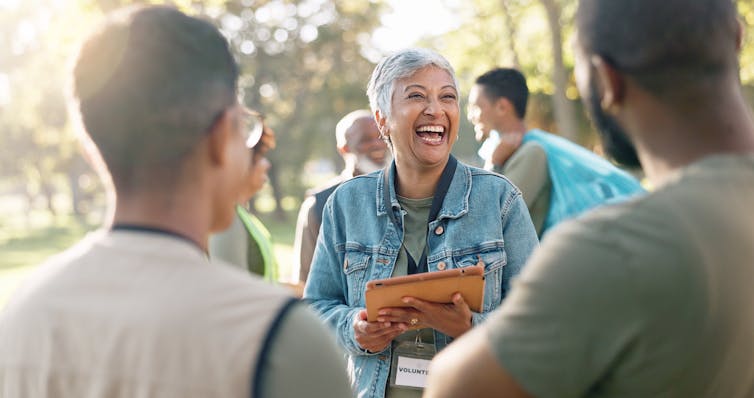 A woman volunteer holding a clipboard greeting people in an outdoor space