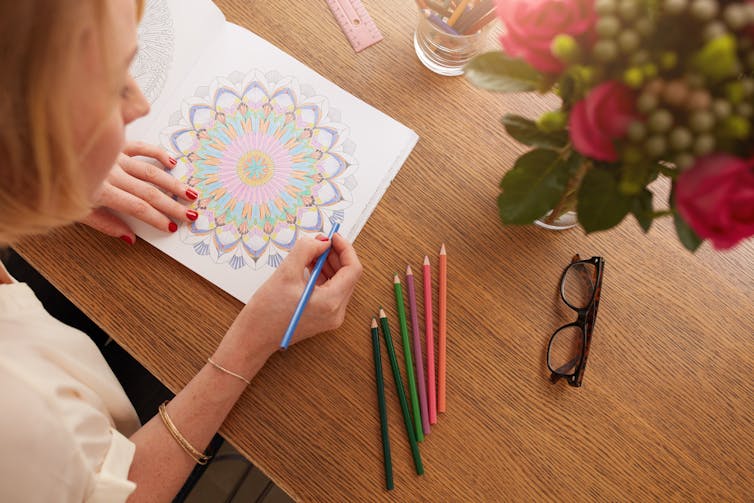 A woman colours on a page with coloured pencils.