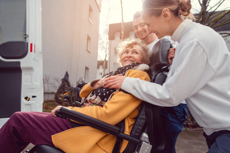 Un homme et une femme accompagnent une femme âgée en fauteuil roulant dans un camion.