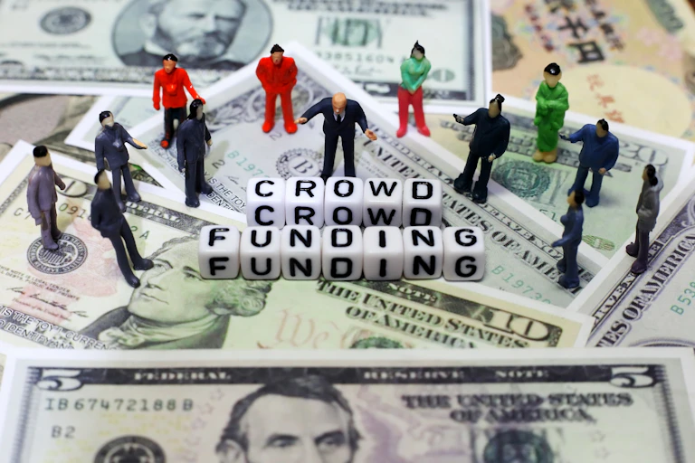 sur un fond de dollars US, des figurines entourent le mot crowsfunding