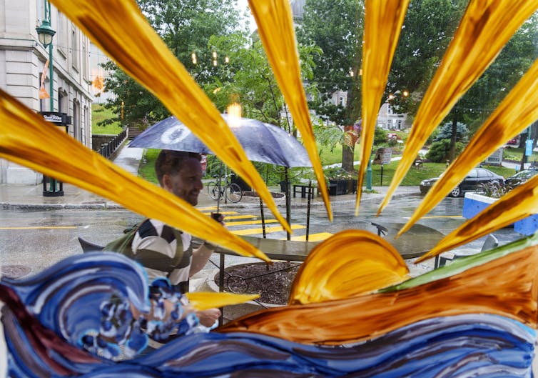 A man holds an umbrella as he walks past the brightly painted window of a cafe.