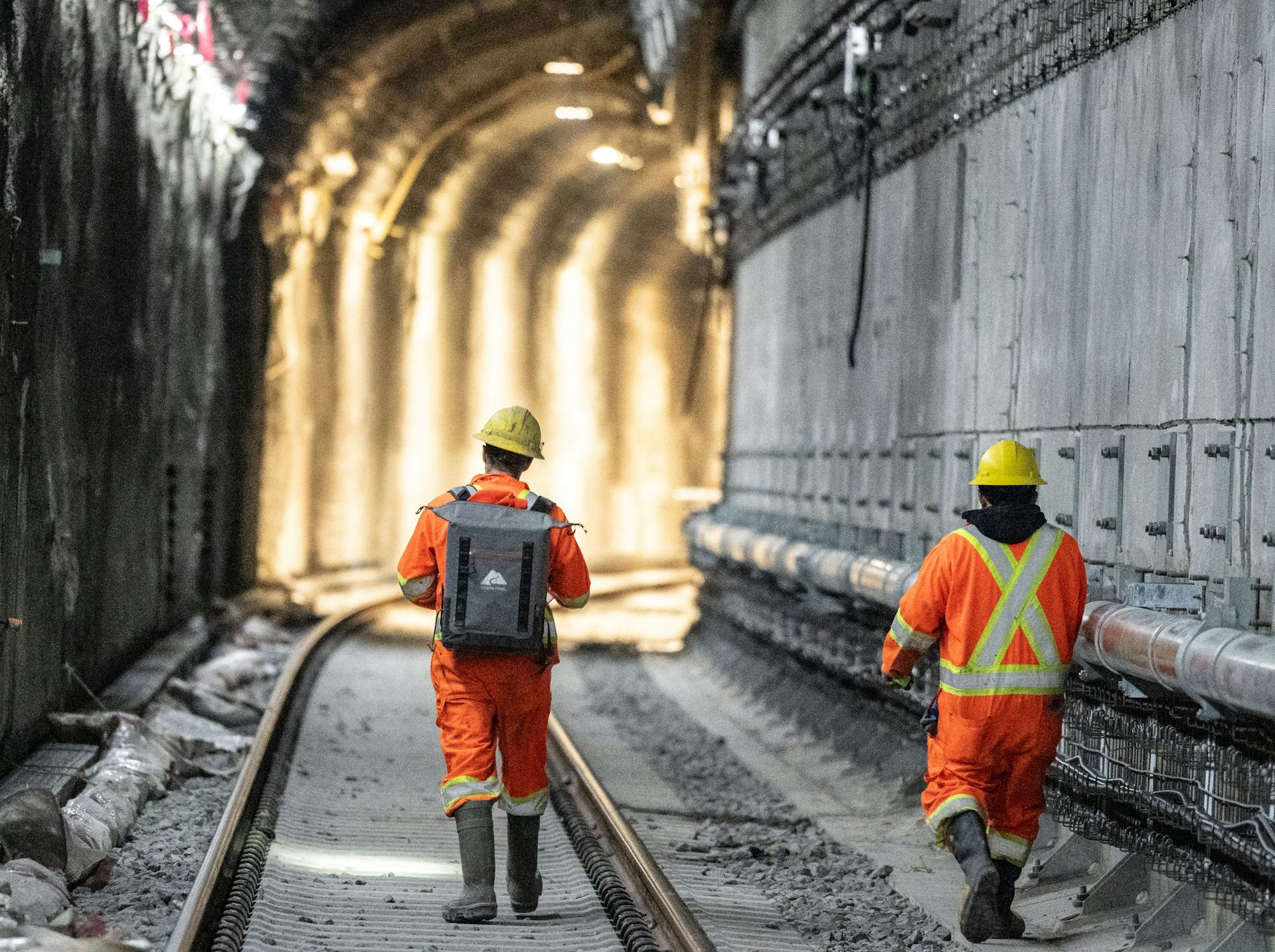 Construction workers in orange work garb walk along light rail tracks.