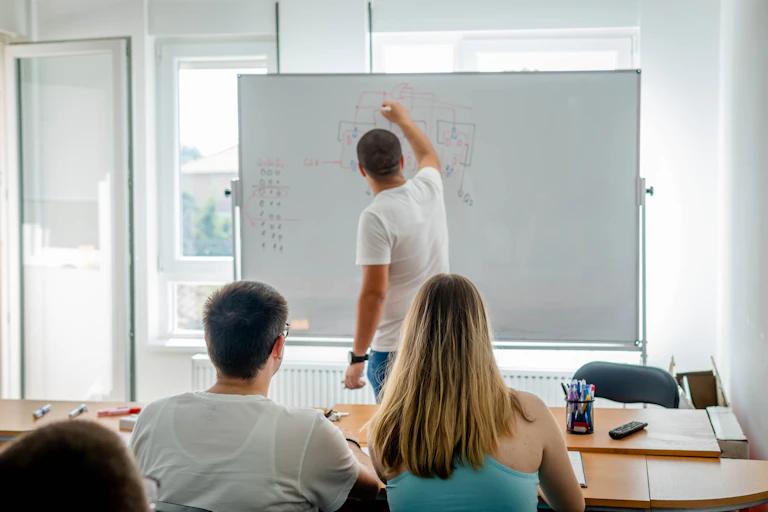 A man writing on a whiteboard in front of a class of students.