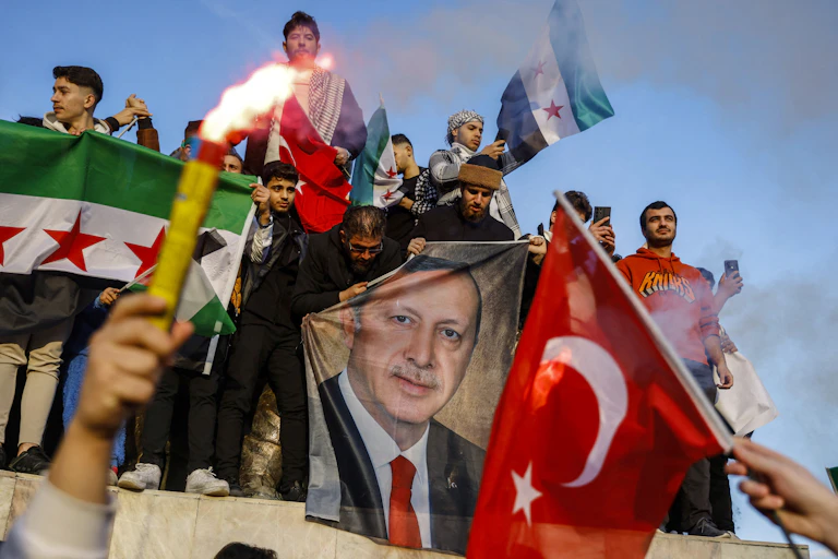 Des manifestants festifs brandissent des drapeaux syriens, turcs et un portrait de Recep Tayyip Erdogan.