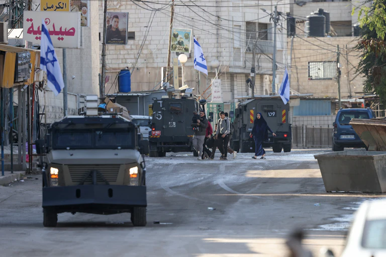 Armored vehicles and blue and white Israeli flags are seen on a street.