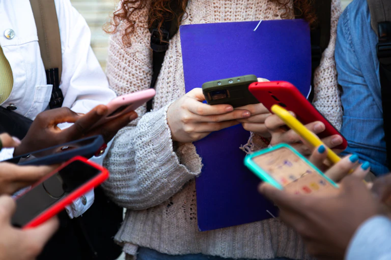 A group of people are seen from below the neck, all holding cellphones, facing one another.