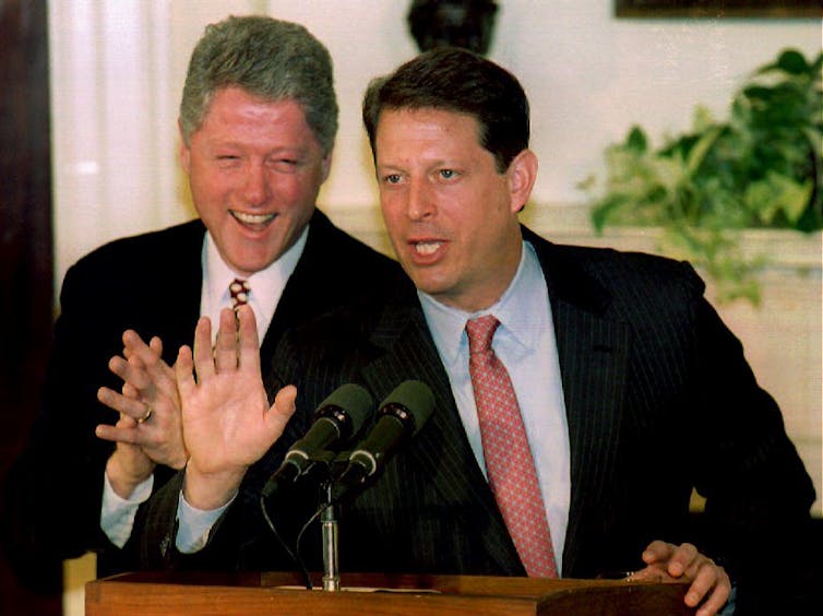 Two men standing behind a microphone at a lectern, looking excited.