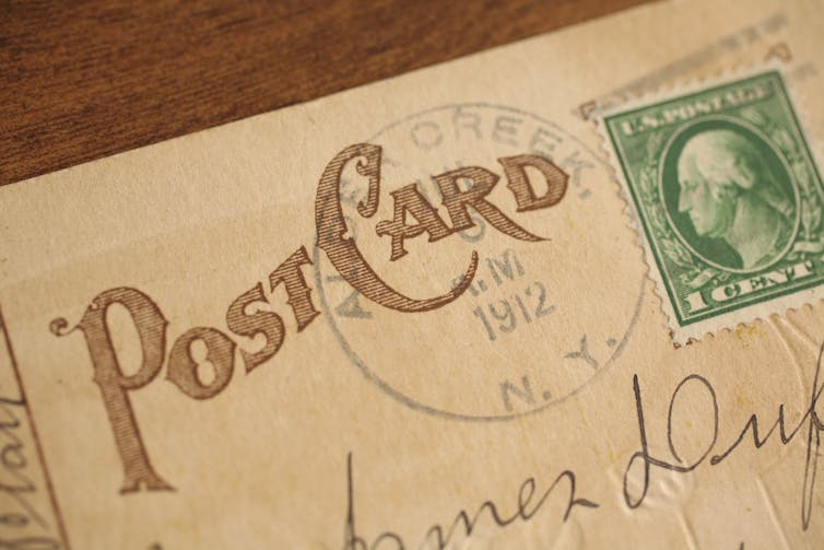 An old postcard looks worn. The year 1912 is visible and there is an old person on the stamp.