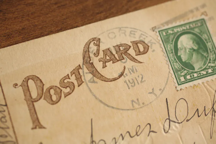 An old postcard looks worn. The year 1912 is visible and there is an old person on the stamp.