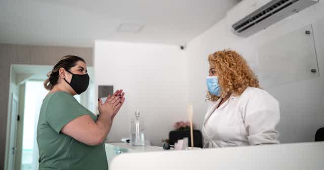 two women wearing face masks speak across a reception desk
