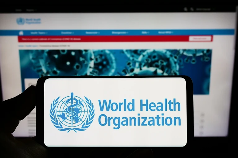 Smartphone with WHO logo held against computer screen showing WHO website