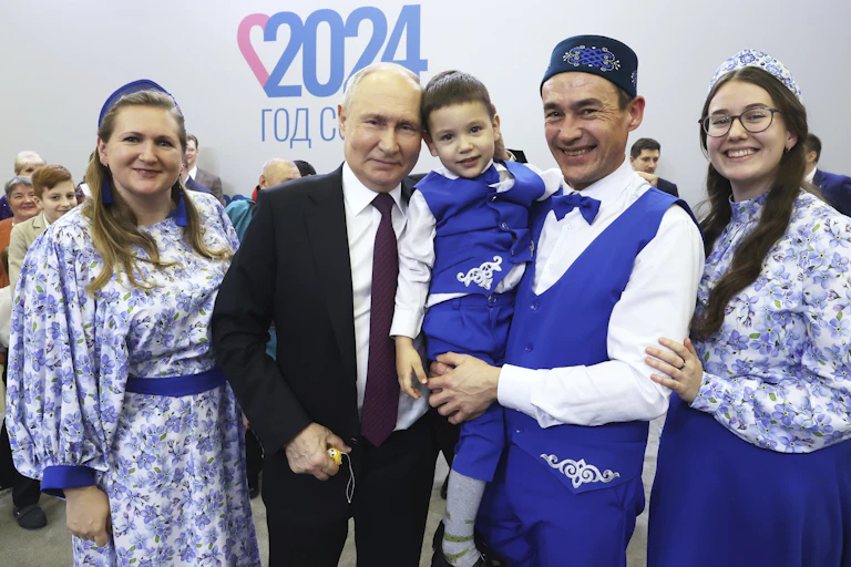 Two women in purple and white dresses and a man holding a young boy pose with a man in a black suit and burgundy tie.
