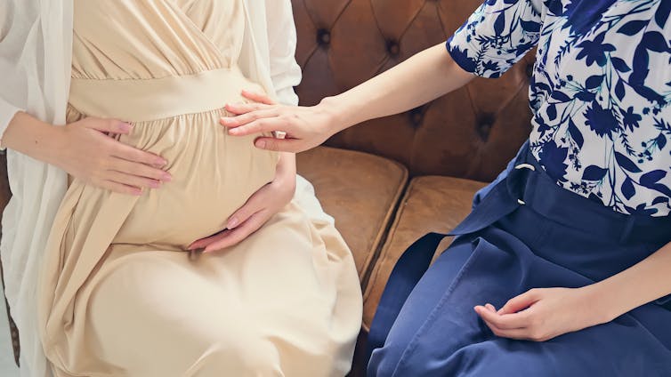 Woman touching a pregnant woman's bump.