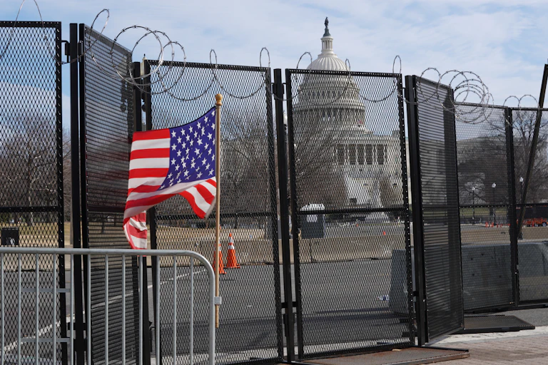 US capitol behind a fence with US flag in foreground.