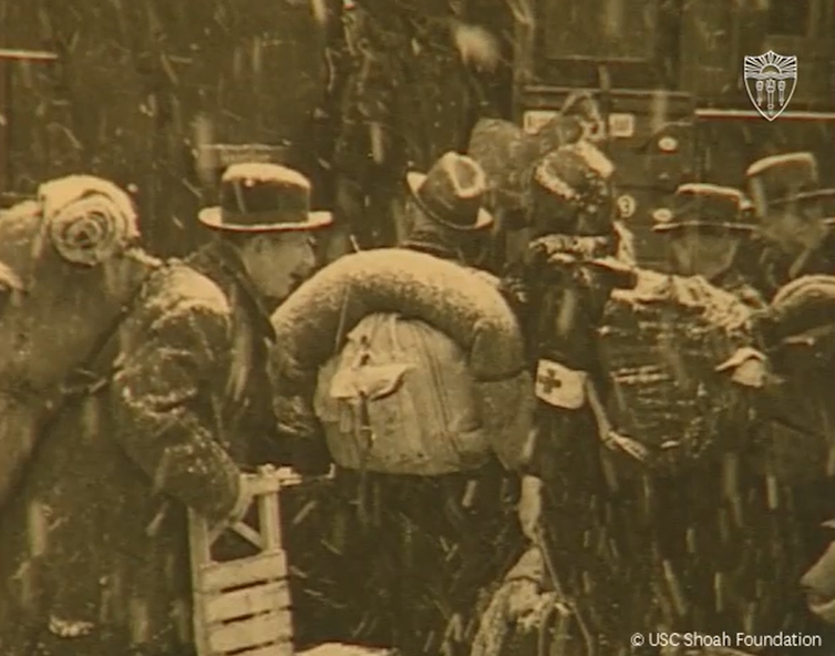 Black and white photo of Jewish people with their belongings boarding a train in heavy snowfall
