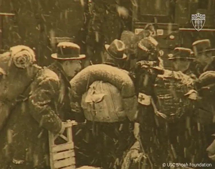Black and white photo of Jewish people with their belongings boarding a train in heavy snowfall