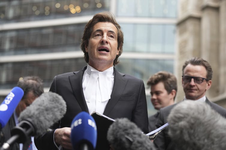 A man in legal robes speaks to the media