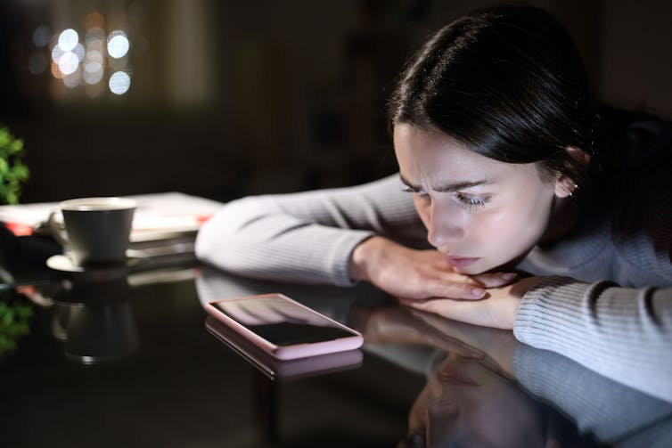 a woman leans on a desk with her phone on the table in front of her