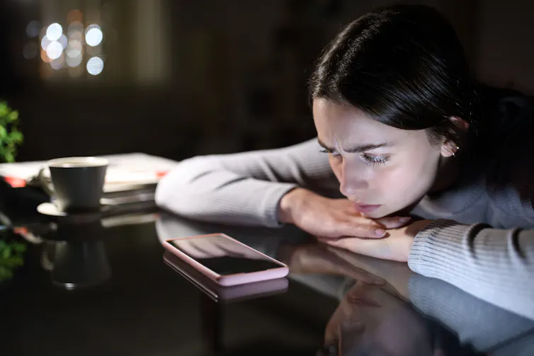 a woman leans on a desk with her phone on the table in front of her