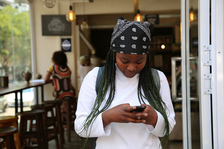 a woman wearing a bandana stares at her phone in her hand