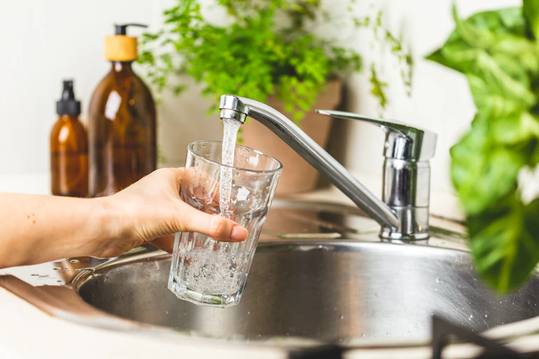 A hand filling a glass of water from the tap.