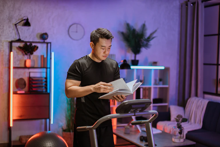 Man reading book while doing fitness exercise, running on treadmill