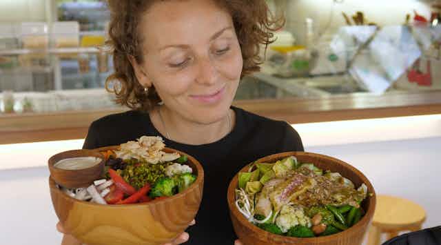 Jeune femme heureuse tenant et représentant deux grands bols remplis de repas végétaliens sains dans un café bio