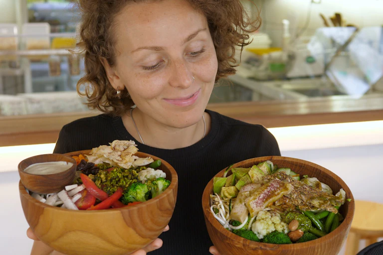 Jeune femme heureuse tenant et représentant deux grands bols remplis de repas végétaliens sains dans un café bio