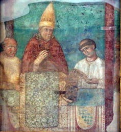 An image in jewel tones of a man in a golden hat and red robes standing on a dais between two other men.