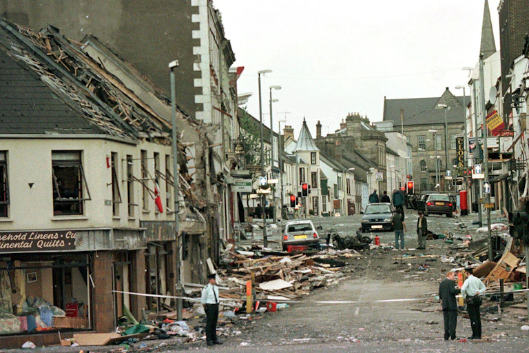 A view down Market Stree in Omagh after it had been blown up by a car bomb. Buildings are falling down and policemen stand by a cordon.
