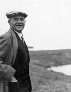 A man in a coat and beret smiles at the camera.