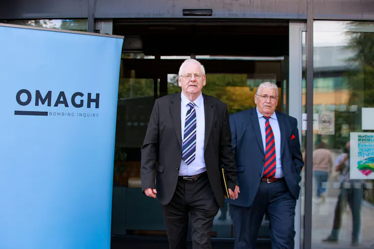 Two men walking past a sign reading 'Omagh Inquiry'