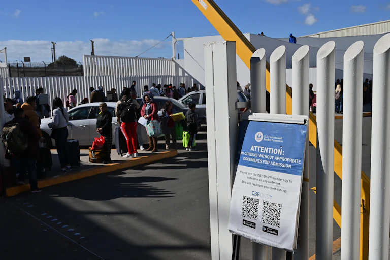 People stand in a long line near a large fence.