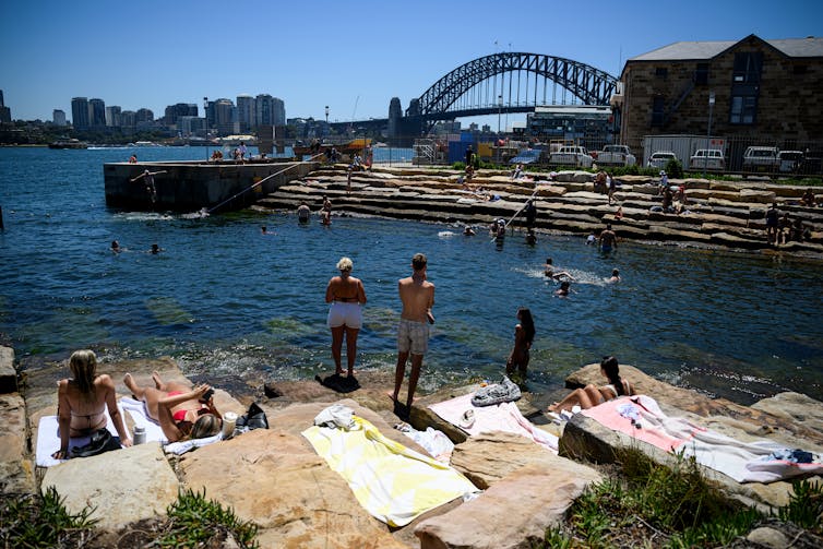 people stand at waters edge in front of bridge