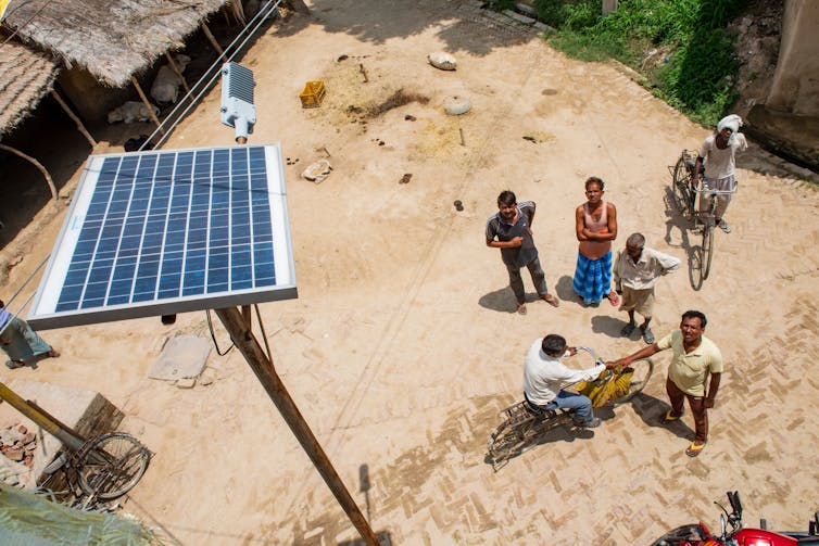 people on dusty ground look up at solar panel