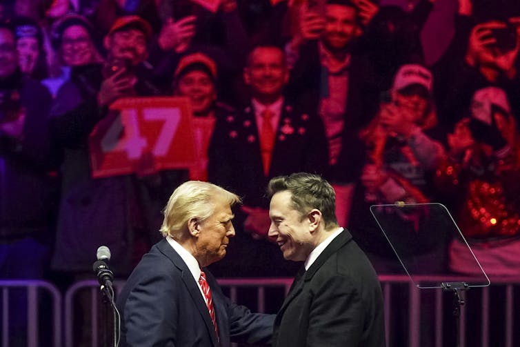 The profiles of two men facing each other in front of a large crowd