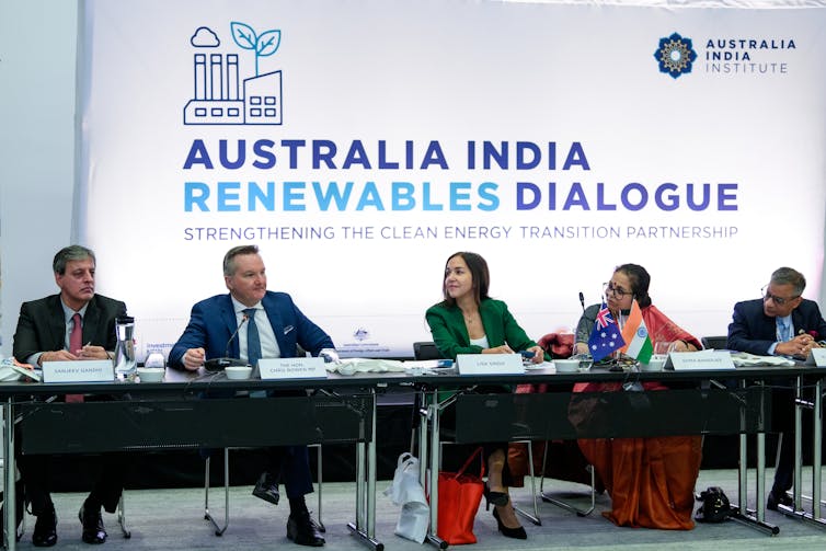 five people sit at tables in front of sign reading 'Australia India Renewables Dialogue'