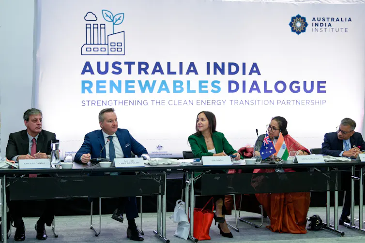 five people sit at tables in front of sign reading 'Australia India Renewables Dialogue'